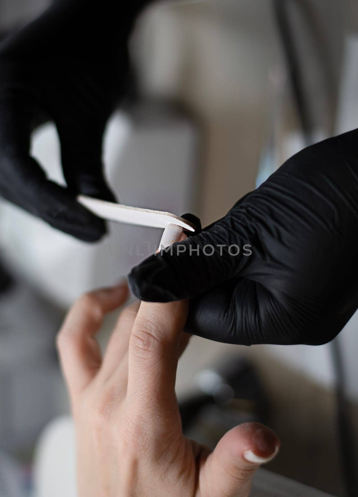 Beauty concept. A manicurist in black latex gloves makes a hygienic manicure, paints the client's nails with gel polish and files them with a nail file in a beauty salon. Close-up. Vertical.