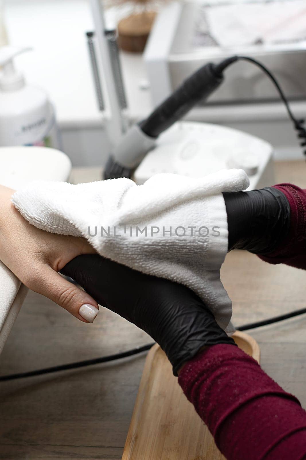 Beauty concept. A manicurist in black latex gloves makes a hygienic manicure, paints the client's nails with gel polish and wipes his hands with a towel in a beauty salon. Close-up. Vertical.