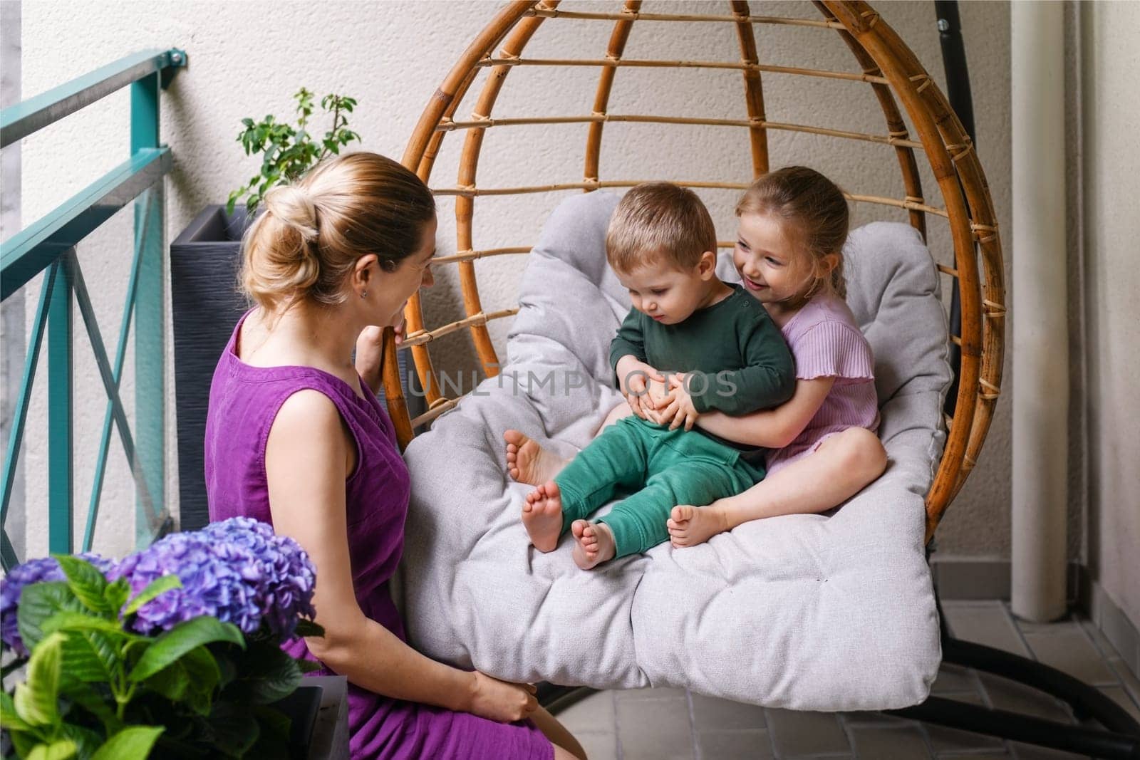 Mother son and daughter are sitting on the balcony with flowers and laughing