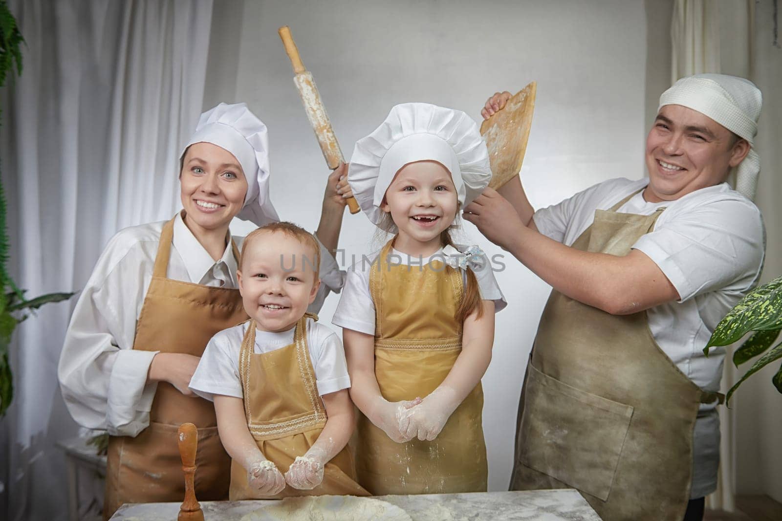 Cute oriental family with mother, father, daughter, son cooking in kitchen on Ramadan, Kurban-Bairam, Eid al-Adha. Funny fighting parents at cook photo shoot. Pancakes, pastries, Maslenitsa, Easter