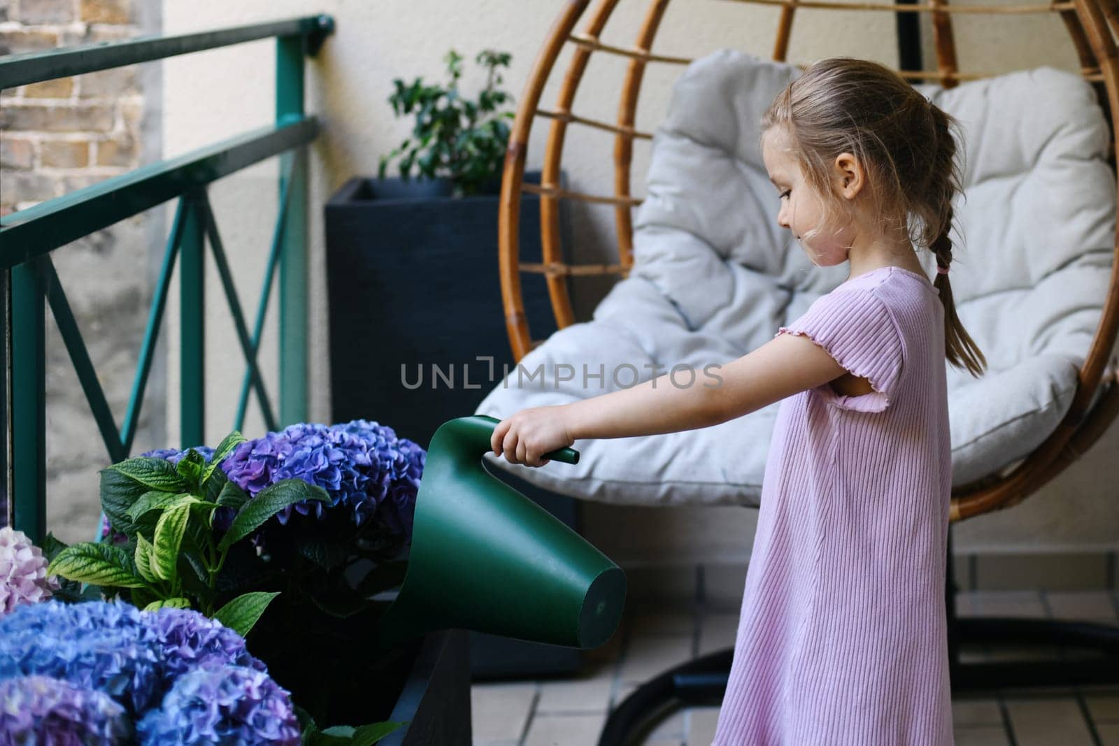 A girl watering hydrangeas on the balcony by Godi