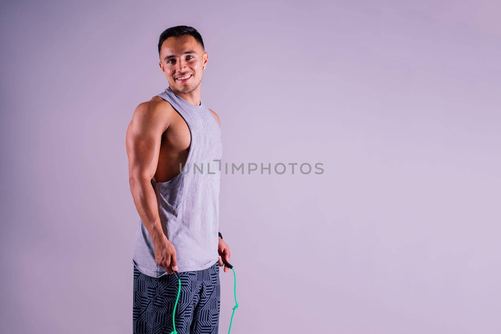 Young man exercising with a skipping rope and looking at the camera isolated on grey background by Zelenin