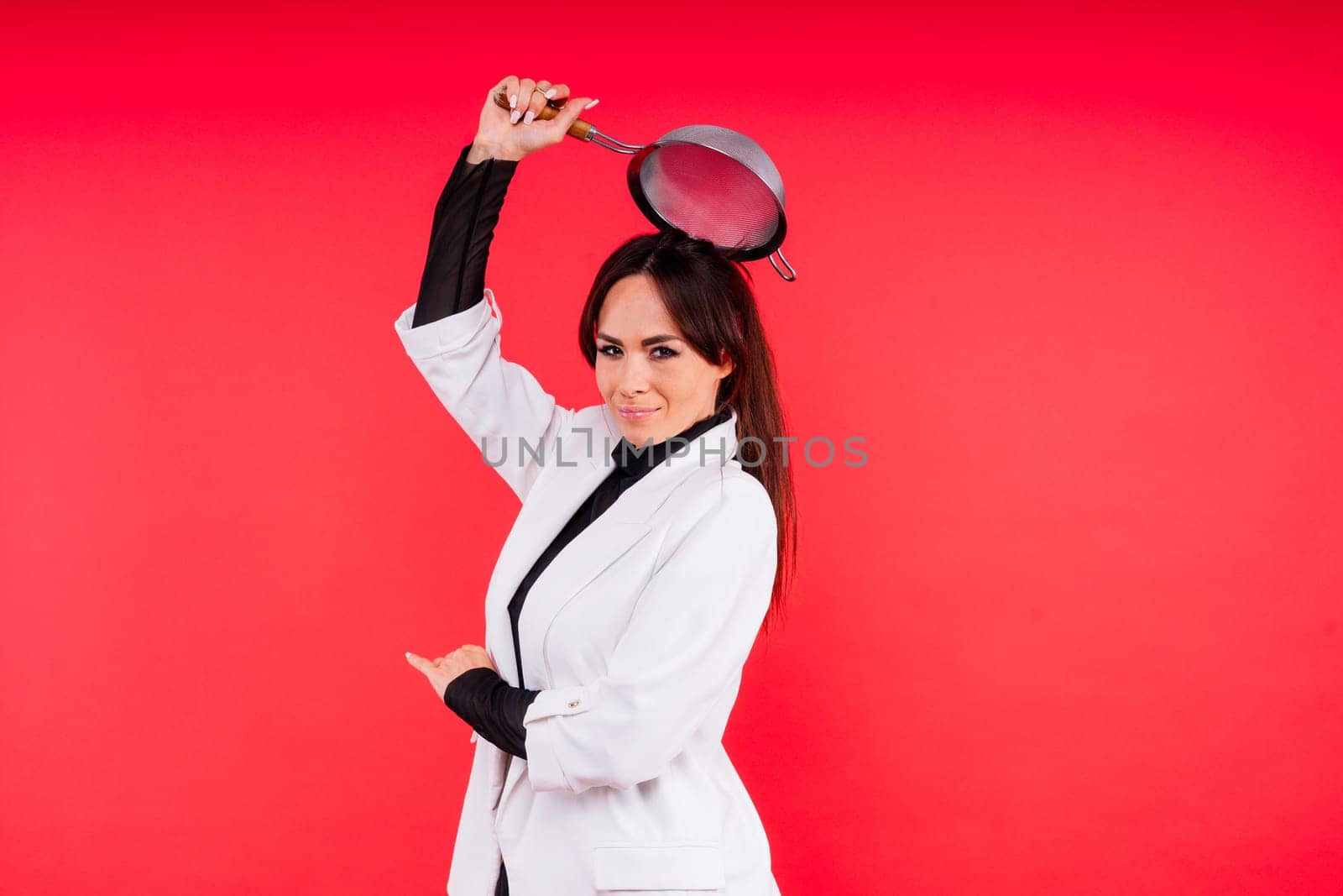 Happy young blonde woman sifts through sieve on red white bsckground in studio