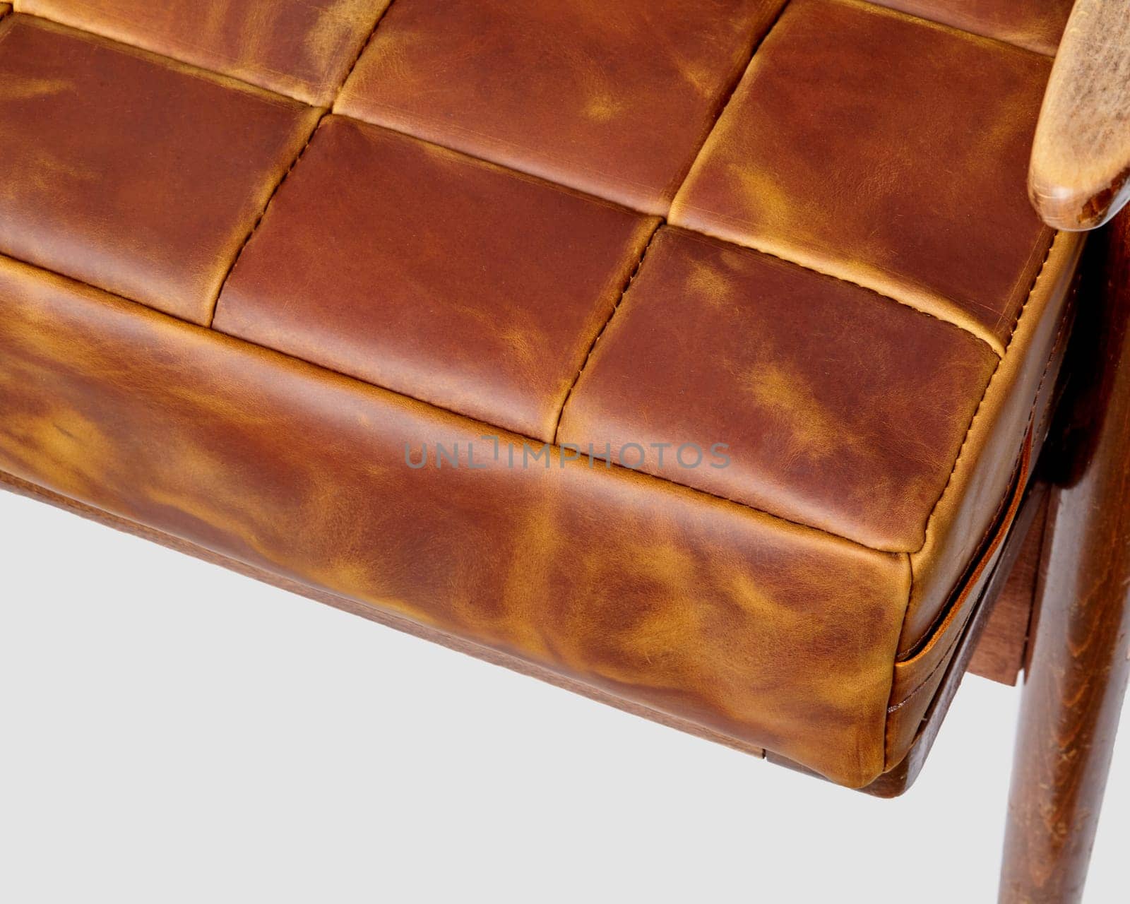 Detailed close-up of rich texture and varied tones of brown leather patchwork seat cushion on vintage style chair with wooden armrest, reflecting skilled craftsmanship