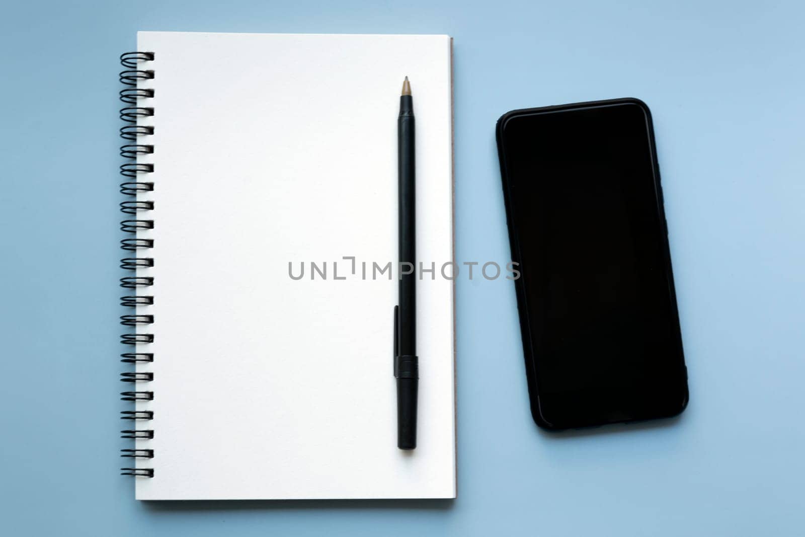 Smartphone with notebook and pen on blue background. Copy space. by JennMiranda