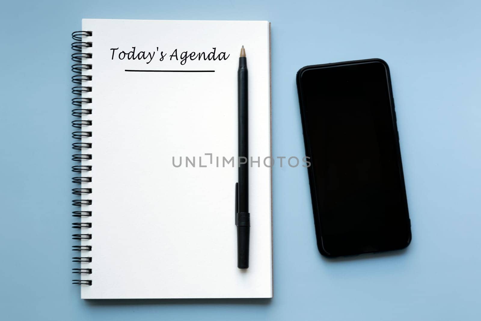 TODAY'S AGENDA written on notebook with pen and smartphone on blue background. by JennMiranda