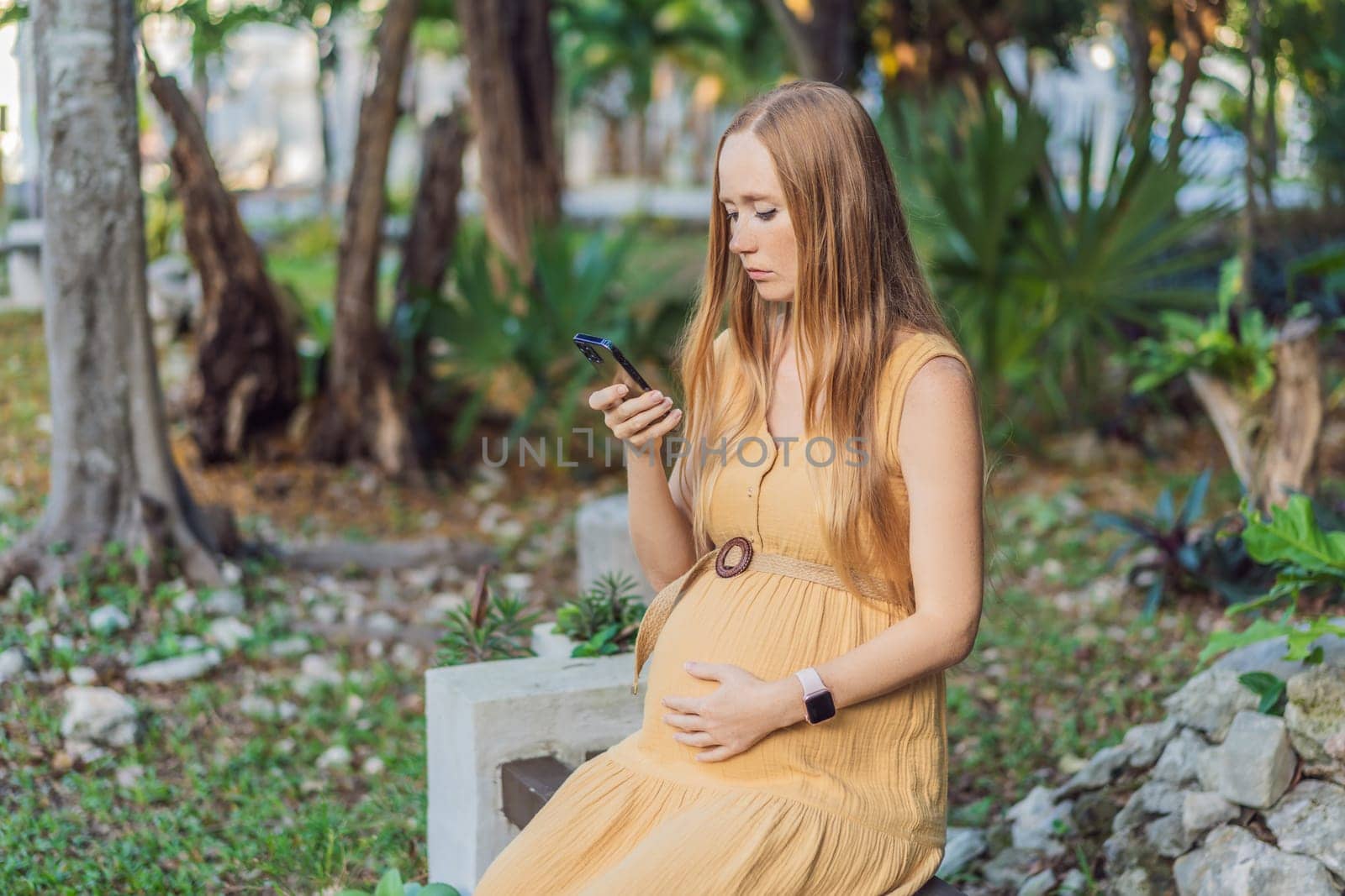 pregnant woman enjoys the tranquility of the park, captivated by her phone, blending the beauty of nature with the modern connection during her pregnancy by galitskaya