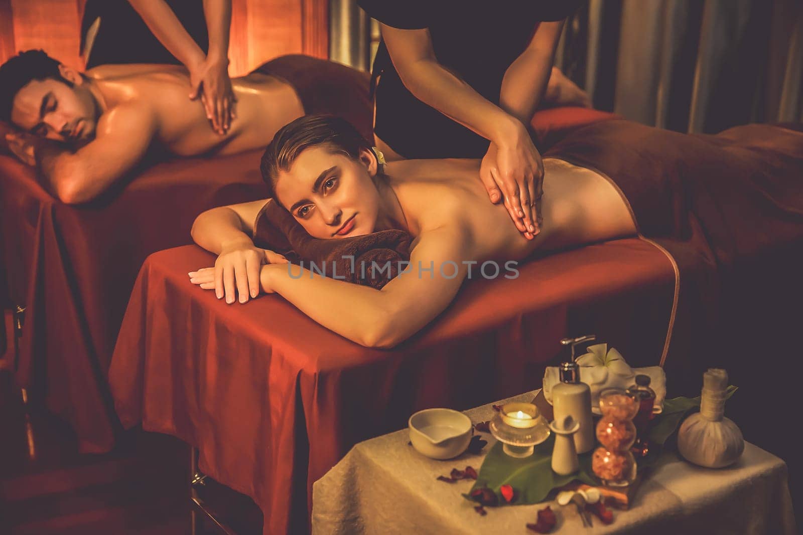 Caucasian couple customer enjoying relaxing anti-stress spa massage and pampering with beauty skin recreation leisure in warm candle lighting ambient salon spa at luxury resort or hotel. Quiescent