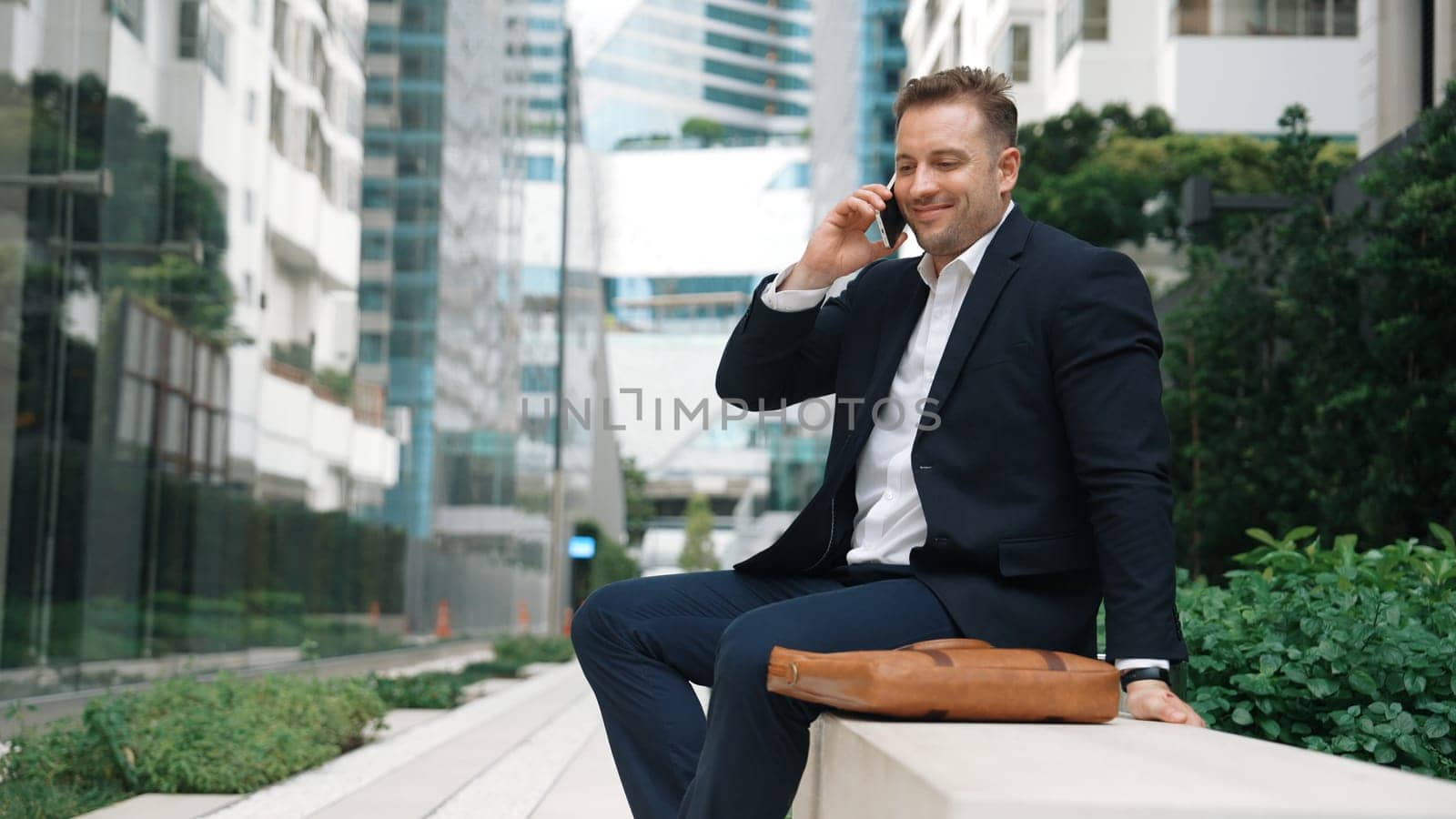 Caucasian businessman sitting at bench while talking to manager by using phone about planning strategy. Professional executive manager calling marketing team and sharing creative idea at city.Urbane.