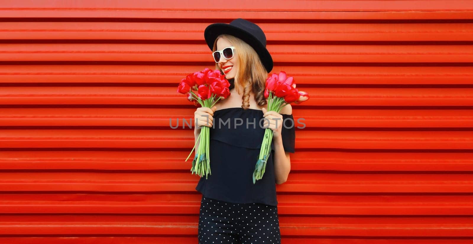 Portrait of beautiful happy smiling woman with bouquet of red rose flowers in black round hat