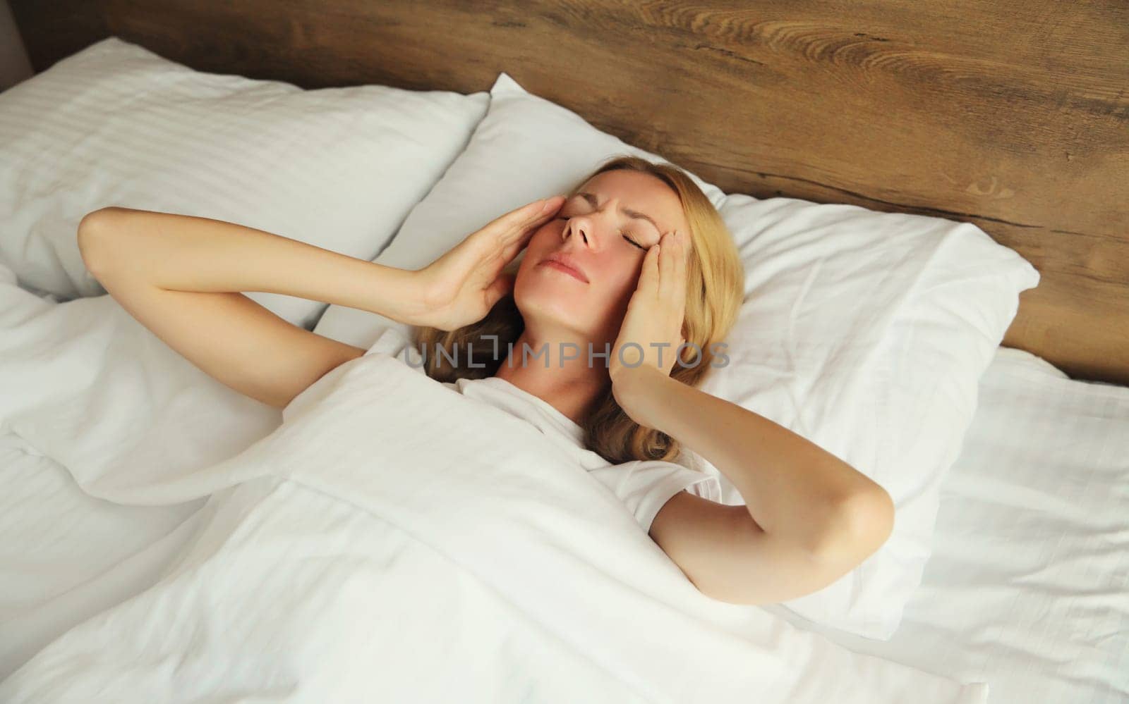 Upset exhausted woman with headache, pain tension in the head, suffers from migraine lying on the bed on pillow in bedroom at home