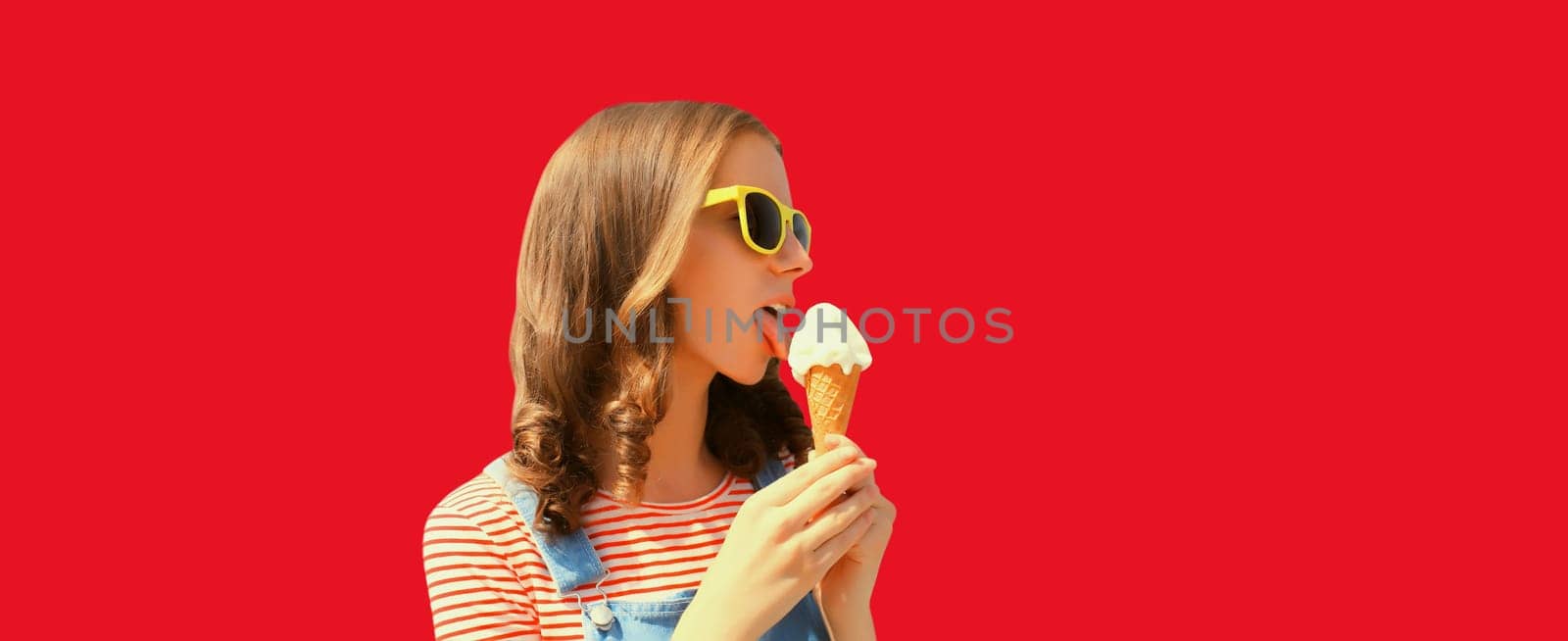 Summer portrait of happy young woman eating ice cream wearing sunglasses on red studio background by Rohappy