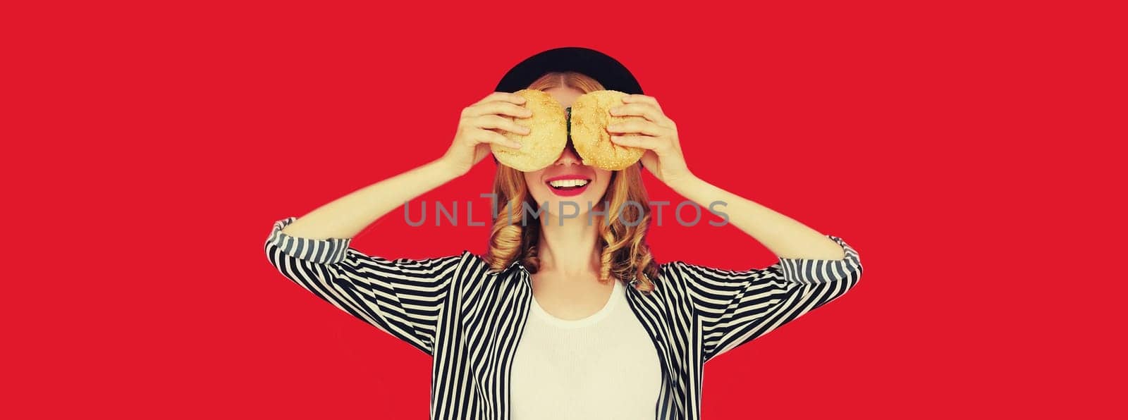 Portrait of happy cheerful young woman having fun with burger fast food isolated on red studio background