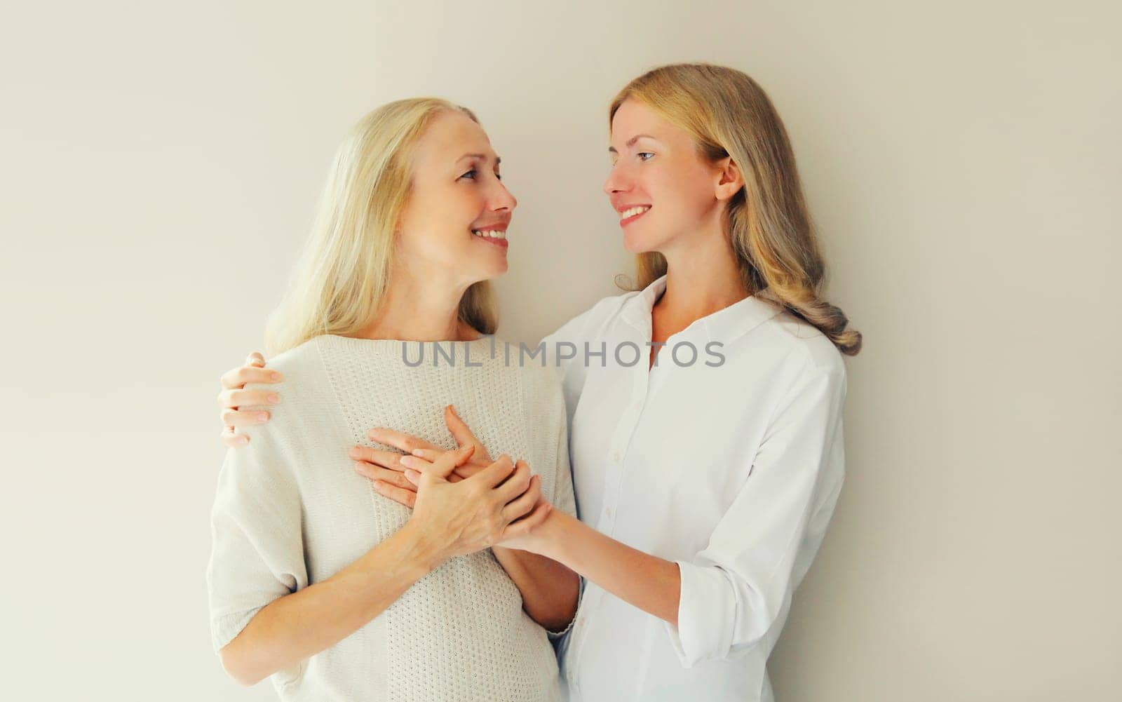 Portrait of happy smiling caucasian middle aged mother or sister and adult daughter together on studio background