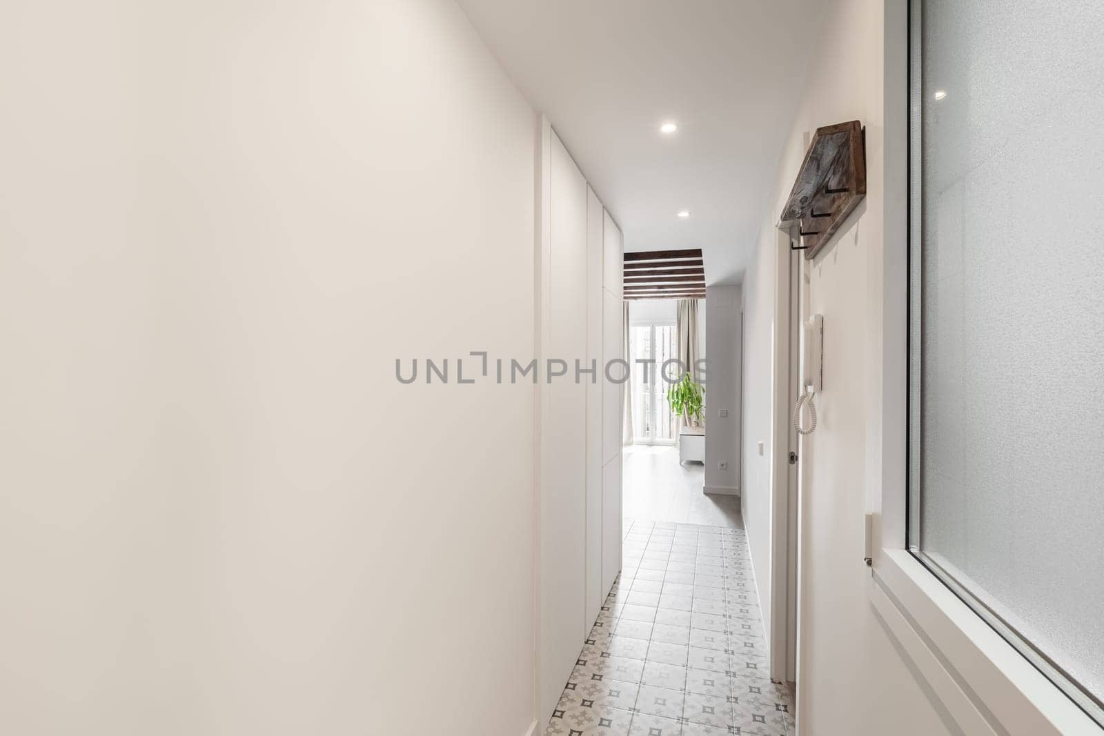 Horizontal shot of a long bright corridor with an entrance door and a view of the living room with a floor-to-ceiling window in an apartment in a new building bought by a young family. Place for text by apavlin