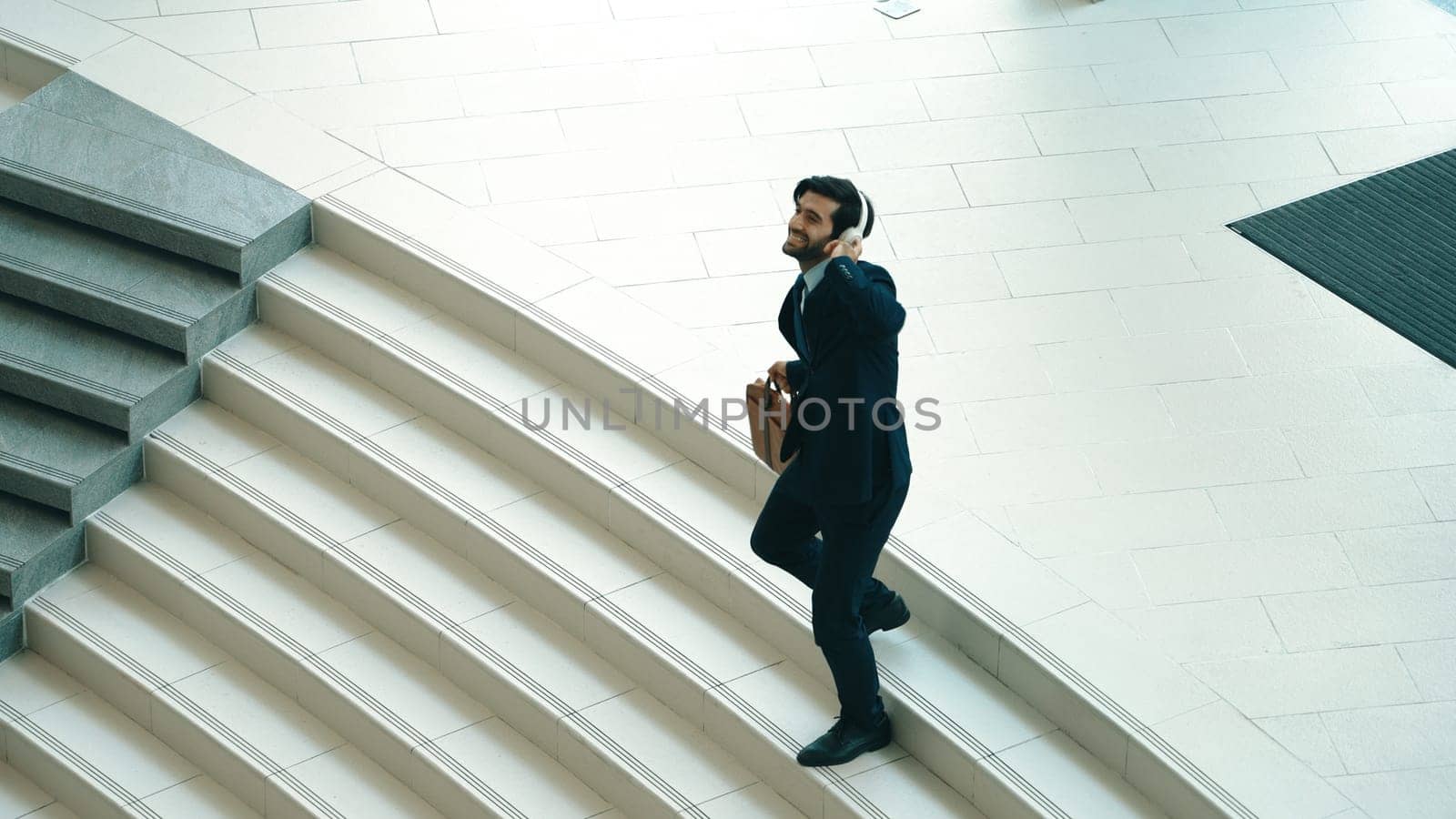 Happy business man listening to music from headphone while walking down at stairs. Executive manager dancing to celebrate increasing sales or successful project or getting new position. Exultant.
