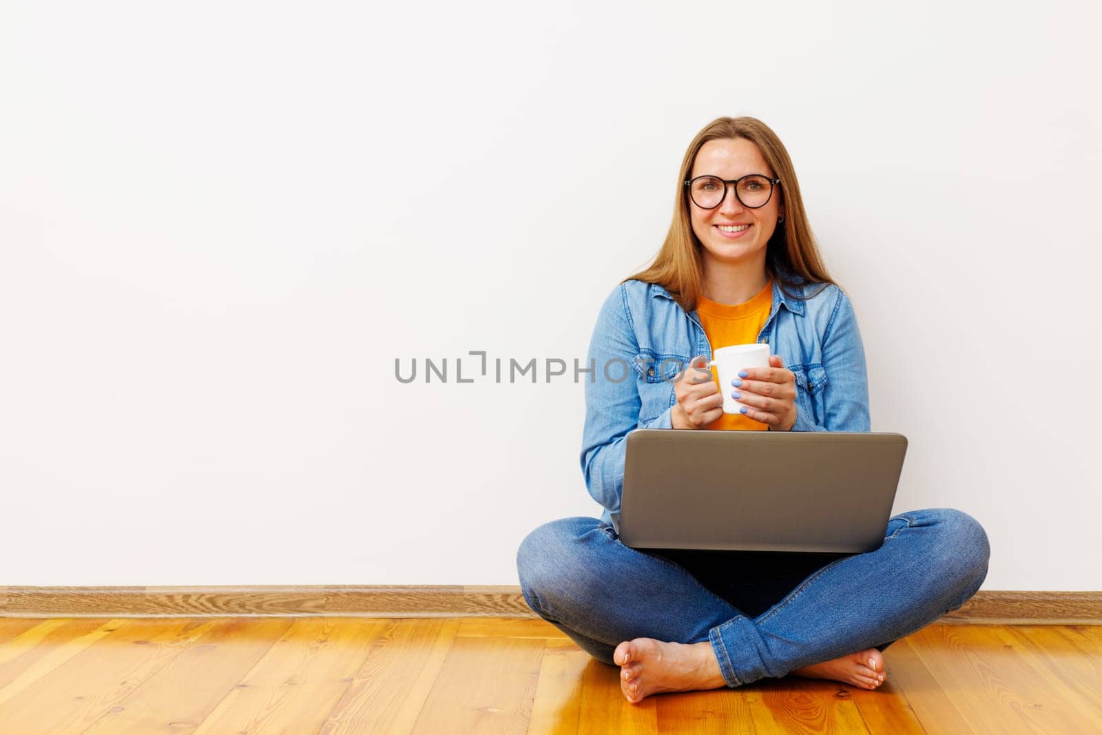 Content Woman with Laptop and Coffee Mug Sitting on Floor.