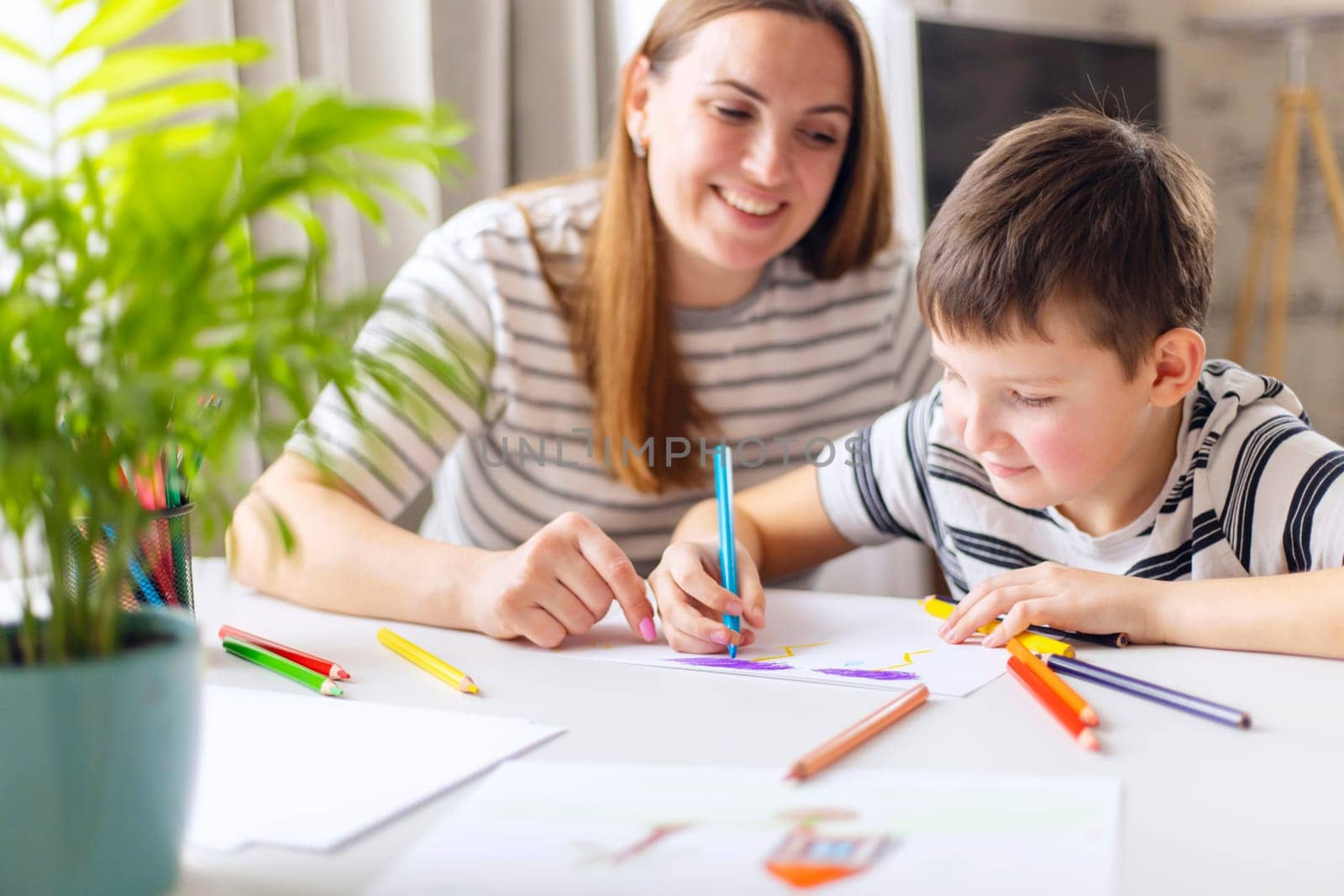 Happy young mother and her son engaged in creative drawing activities at home, surrounded by colorful pencils.