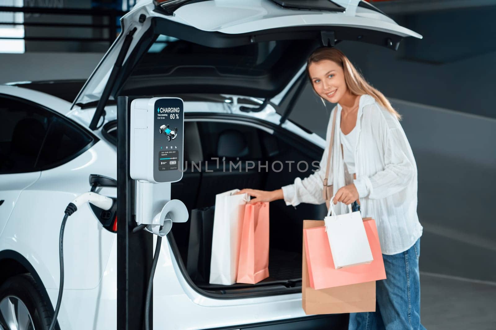 Young woman travel with EV electric car to shopping center parking lot charging in downtown city showing urban sustainability lifestyle by green clean rechargeable energy of electric vehicle innards