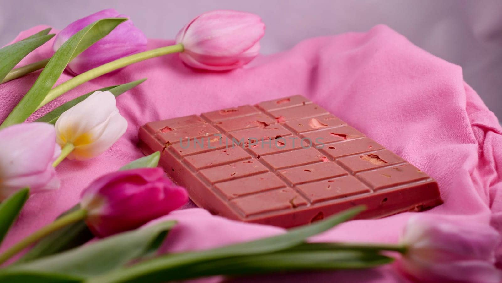 A bar of pink ruby chocolate with sublimated freeze-dried strawberries and almonds and spring tulip flowers . A dessert based on berries and nuts for International Women's Day, March 8, mother's day