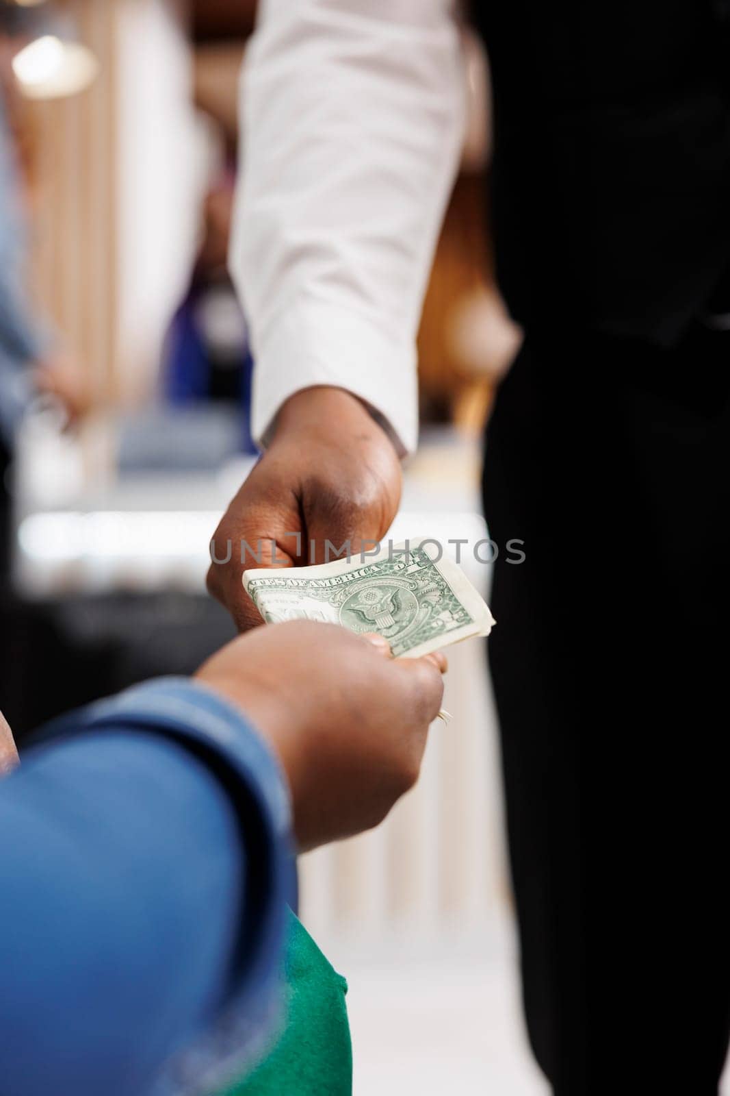 Close up of male African American waiter receiving tip from generous hotel guest. Tourist giving money cash to restaurant worker, making order, paying bill. Tipping in hospitality industry