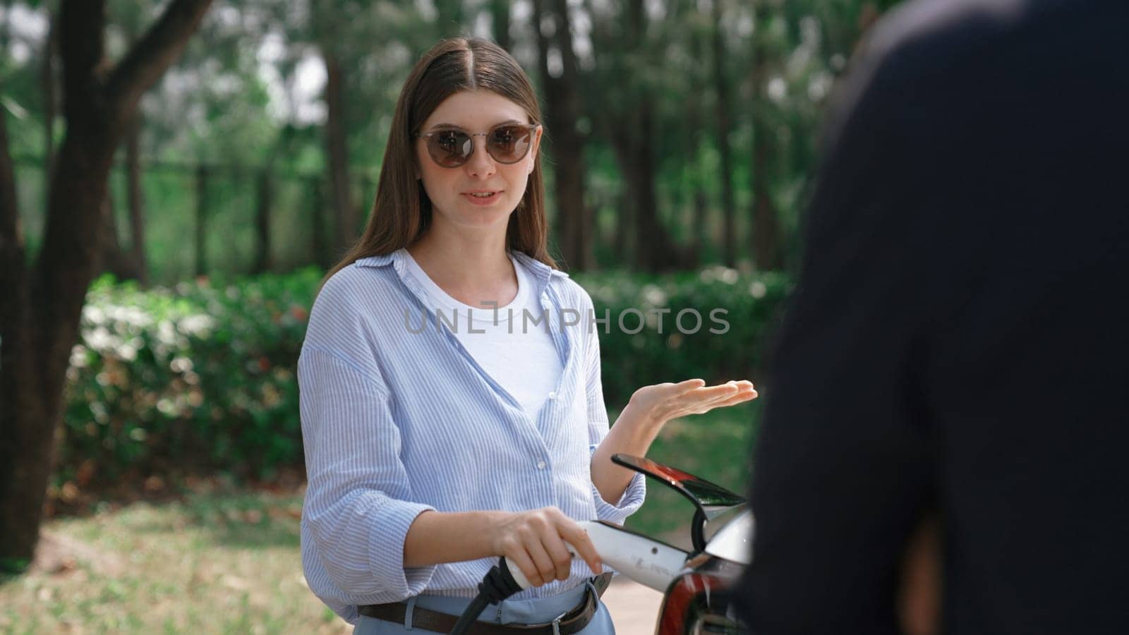 EV car recharging electricity for battery by lovey couple traveling during their road trip travel by eco friendly electric vehicle in national park and greenery forest on holiday. Exalt