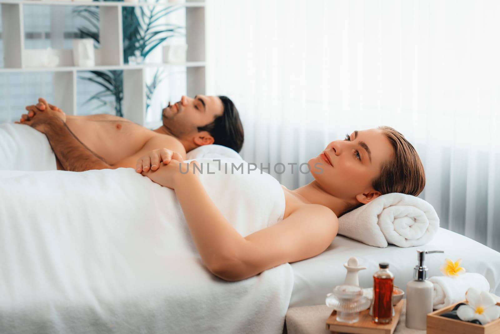 Caucasian couple customer enjoying relaxing anti-stress spa massage and pampering with beauty skin recreation leisure in day light ambient salon spa at luxury resort or hotel. Quiescent