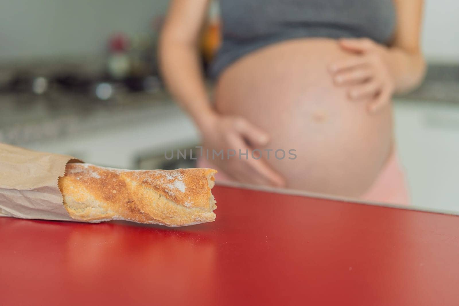 Pregnant woman eating bread in the kitchen. Exploring the impact of gluten during pregnancy: understanding the potential benefits and risks for maternal health and fetal development.