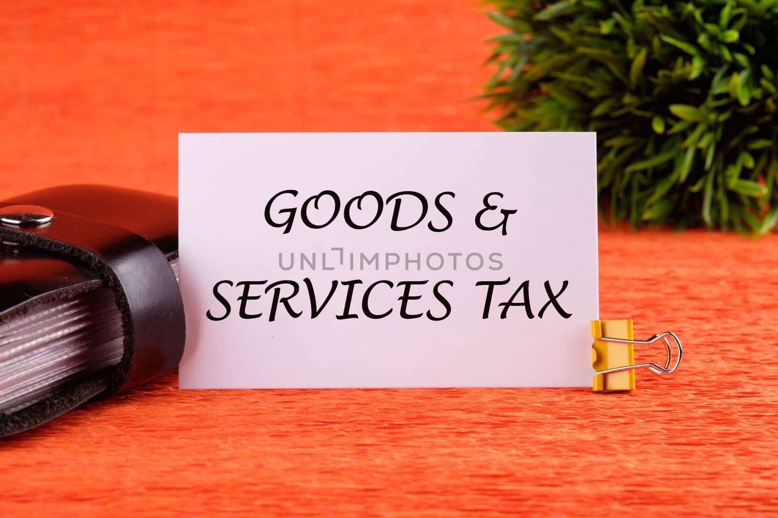 Goods and services and tax text written on a white card near the business card holder in black on an orange background
