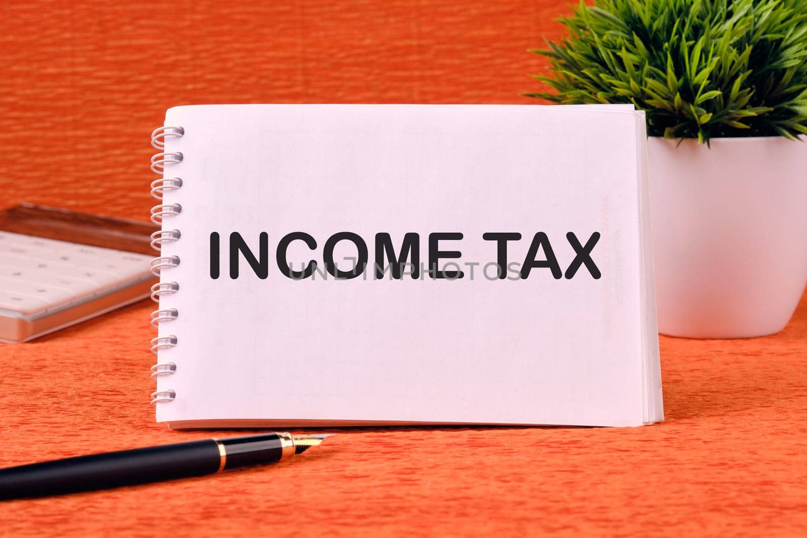 INCOME TAX text written on a blank sheet of notepad, there is a calculator, a pen and a flower in the background