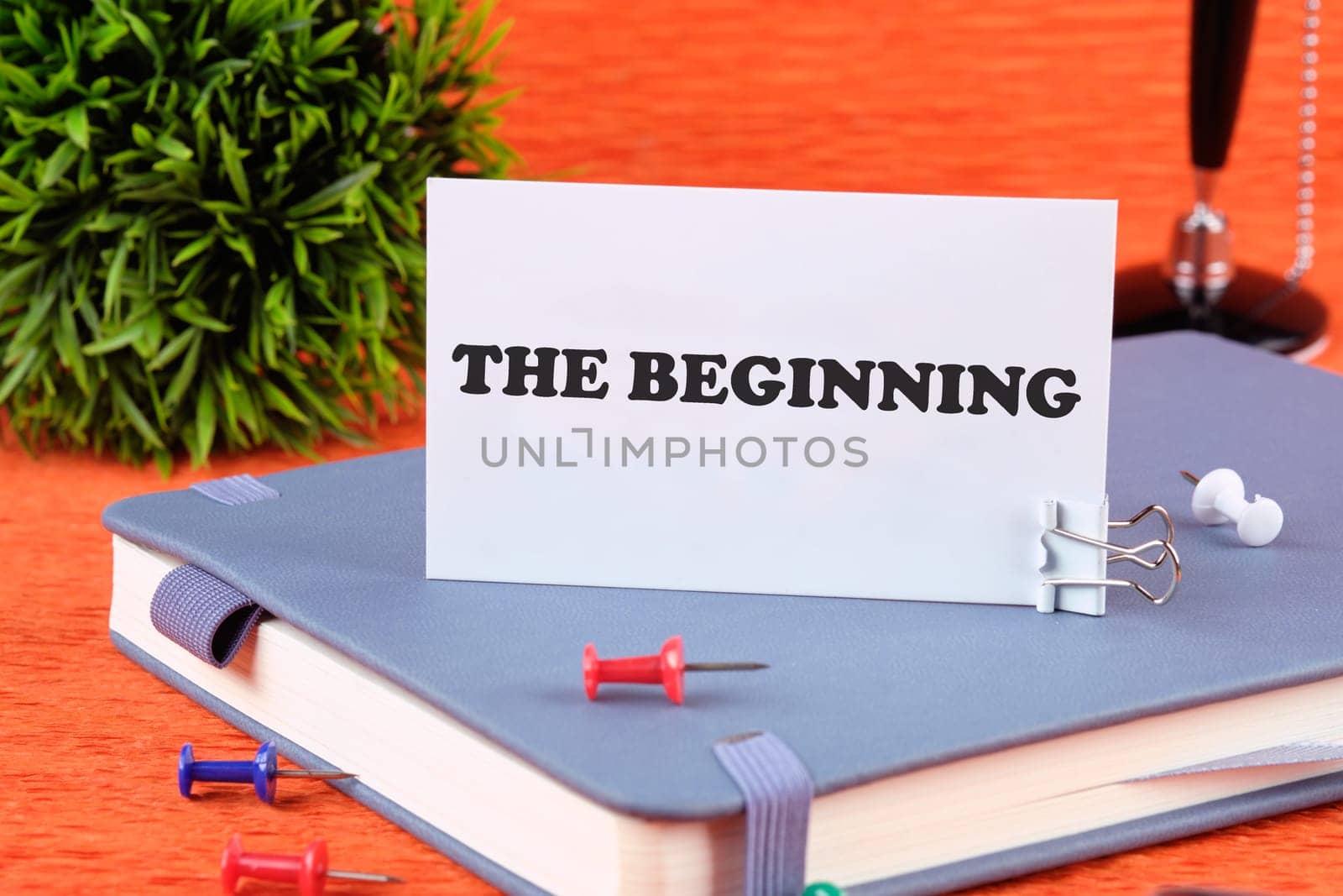 The beginning text written on a business card standing with a clip on a diary, a notebook on an orange background