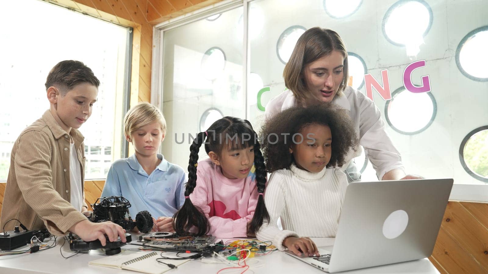 Caucasian teacher praise student while looking at learner work or presentation. Group of diverse student looking at presentation and fixing motherboard at table with chips and wires placed. Erudition.