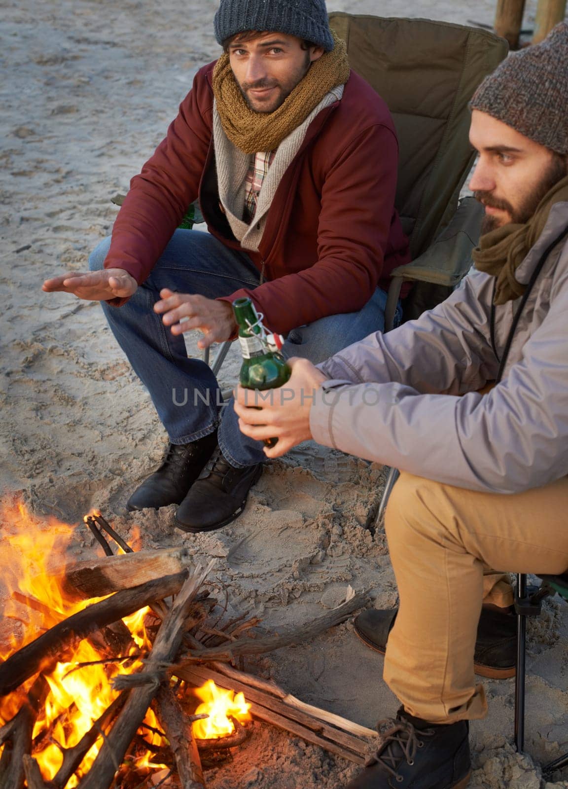 Men, sunset and campfire with portrait, smile and beer with travel adventure and journey outdoor. Friends, ocean and sea with bonding, winter and vacation by the beach together on holiday with fire.