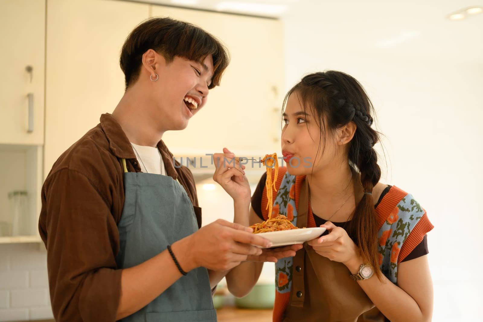 Happy young lovers eating bolognese spaghetti in kitchen. Love, relationships and food concept by prathanchorruangsak