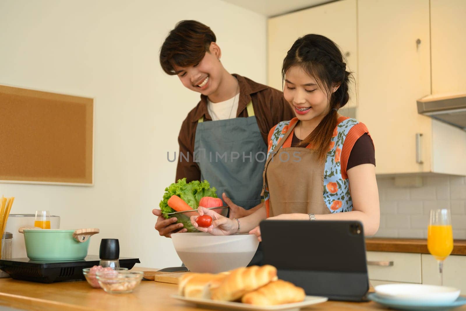 Young couple reading recipe from internet on digital tablet while cooking healthy food together in kitchen.