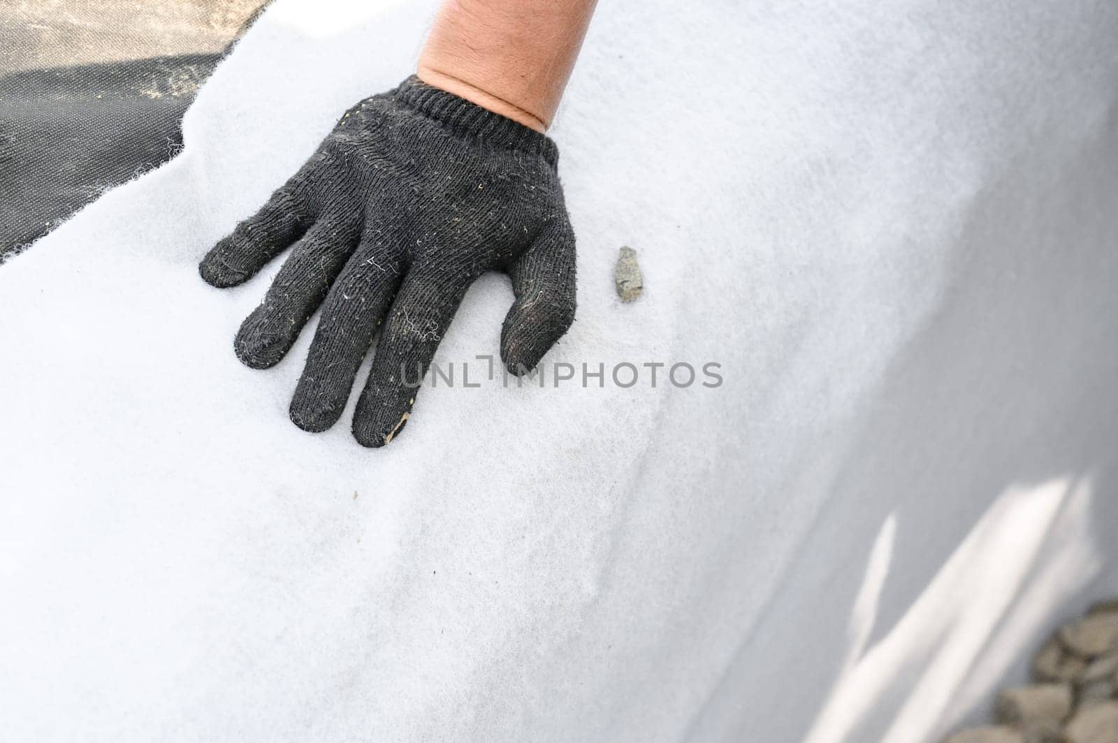 The craftsman spreads white geotextile in the trench. A mans hand in black gloves on a white canvas.