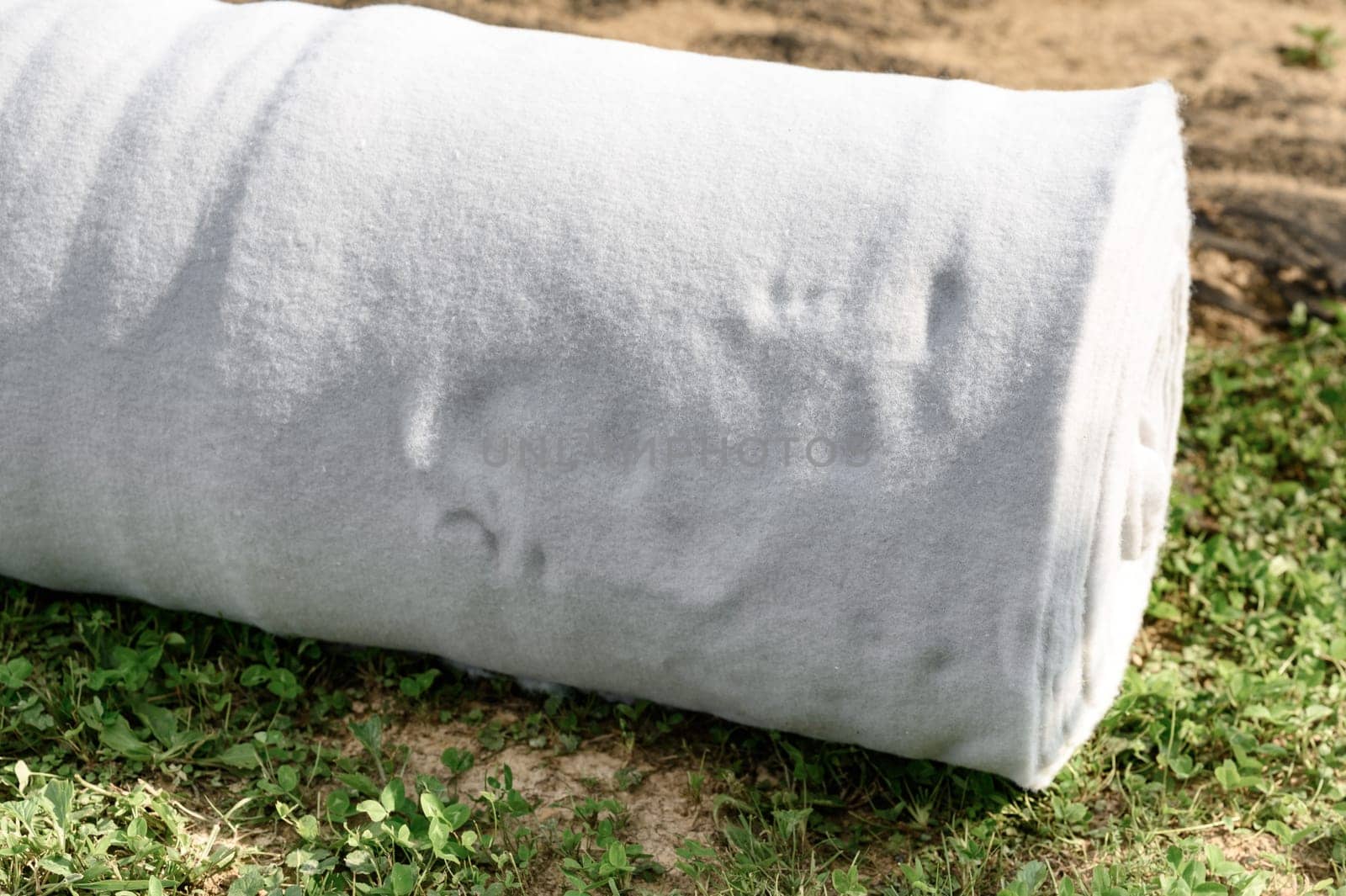 A roll of white geotextile lies on a field. Preparation for drainage works.