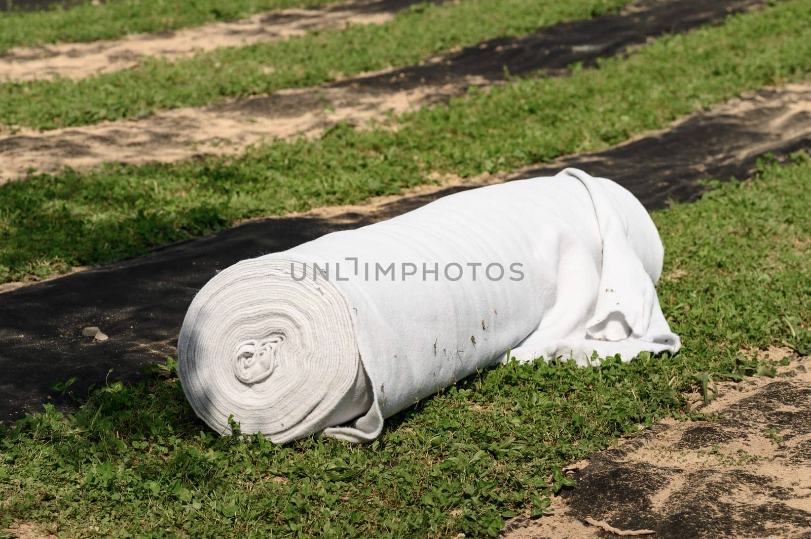 A roll of white geotextile lies on field. Preparation for drainage works. by Niko_Cingaryuk