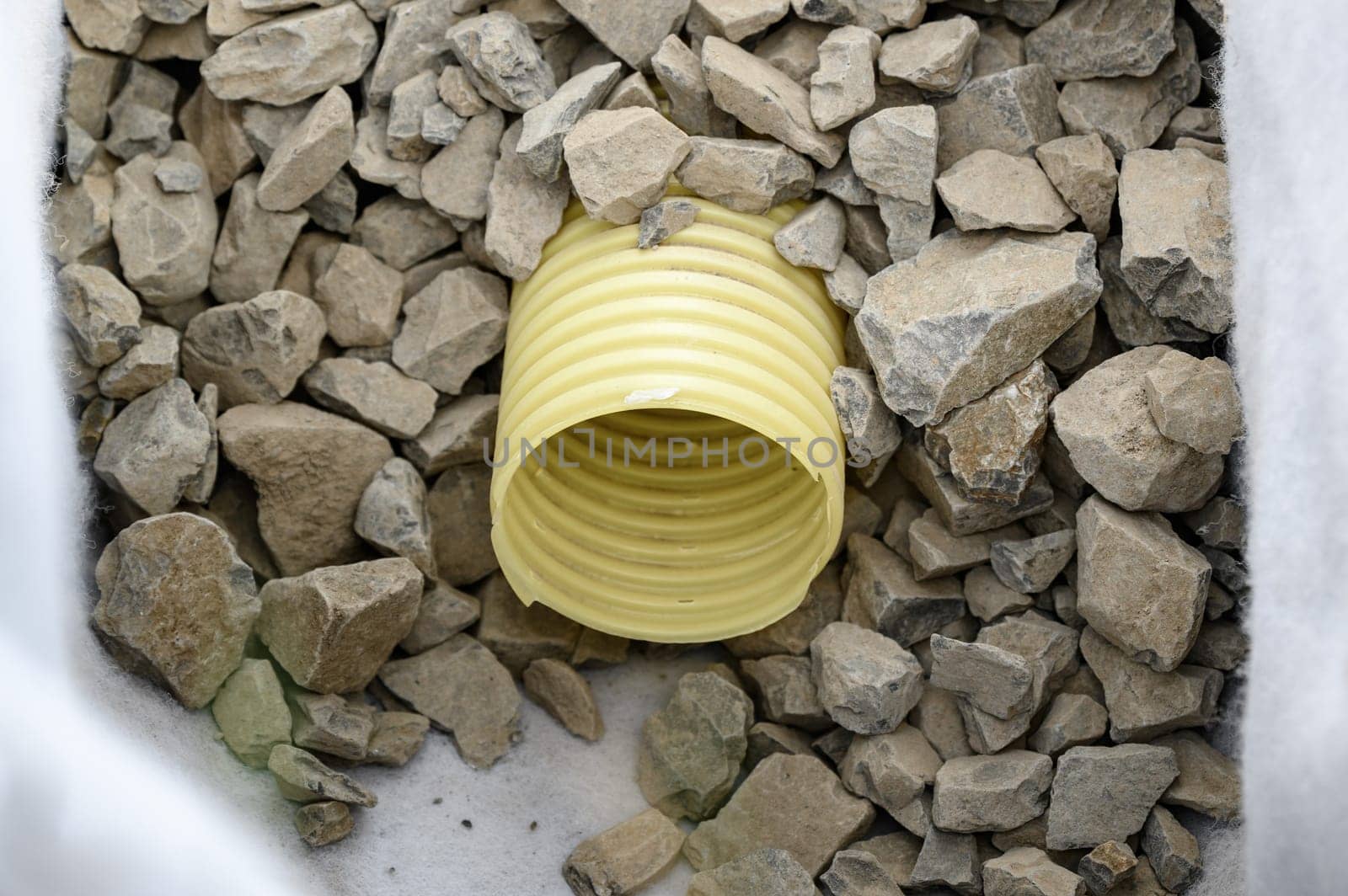 Yellow corrugated pipe with perforation in a trench with crushed stone and geotextile. Drainage works for the removal of ground water. by Niko_Cingaryuk