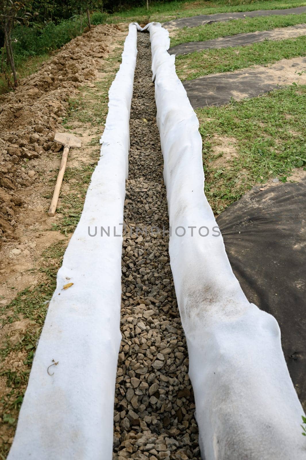 The drainage trench is covered with geotextile and filled with crushed stone to drain ground water from the site. by Niko_Cingaryuk