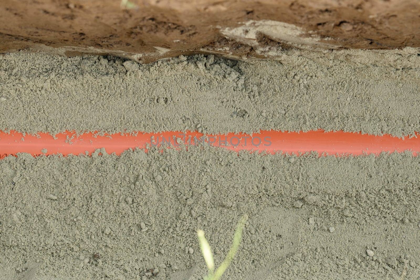 An orange reinforced sewer pipe is compacted with sand in a trench. Plumbing works on a private plot.
