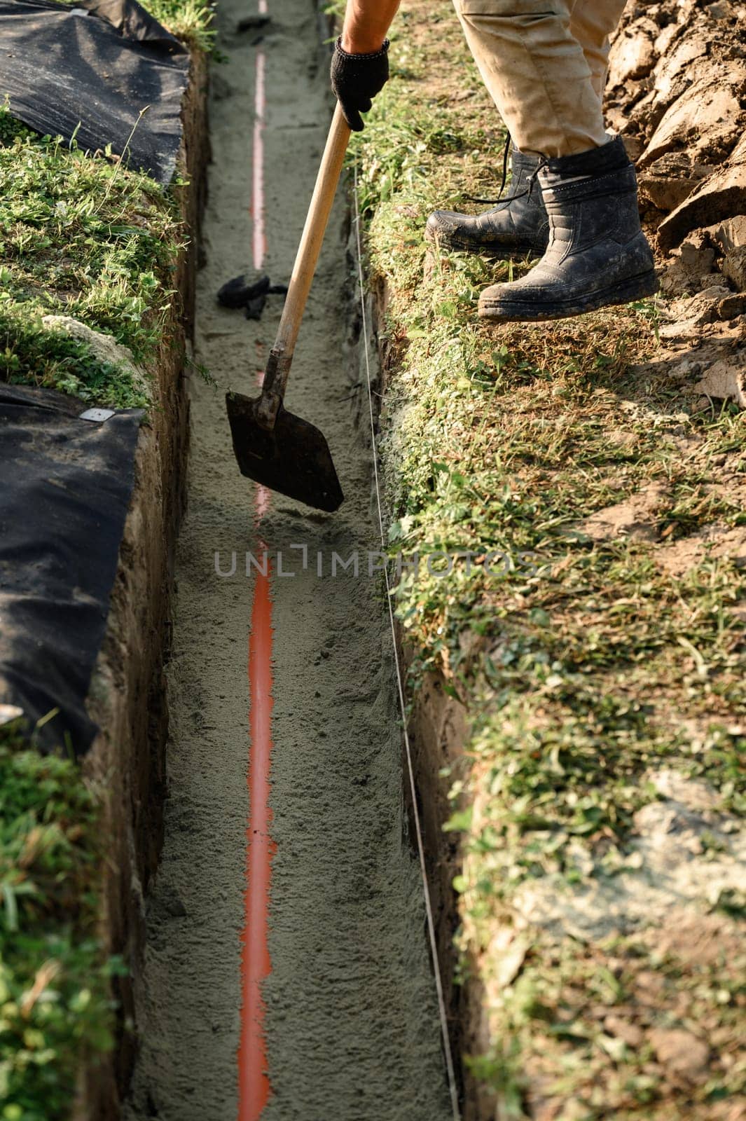 A plumber installs a reinforced orange sewer pipe during site maintenance.