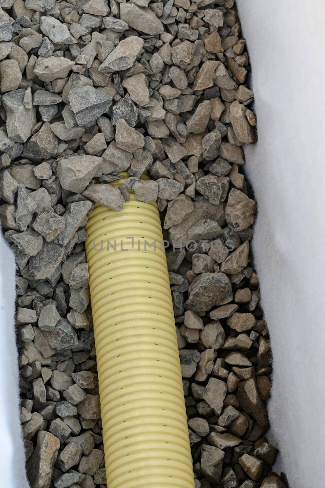 Yellow corrugated pipe with perforation in a trench with crushed stone and geotextile. Drainage works for the removal of ground water. by Niko_Cingaryuk