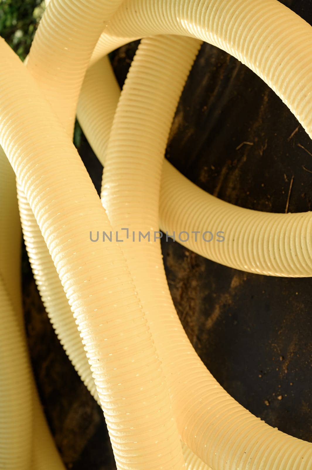 Perforated yellow drainage pipe with slots in a roll twisted in a spiral close up.