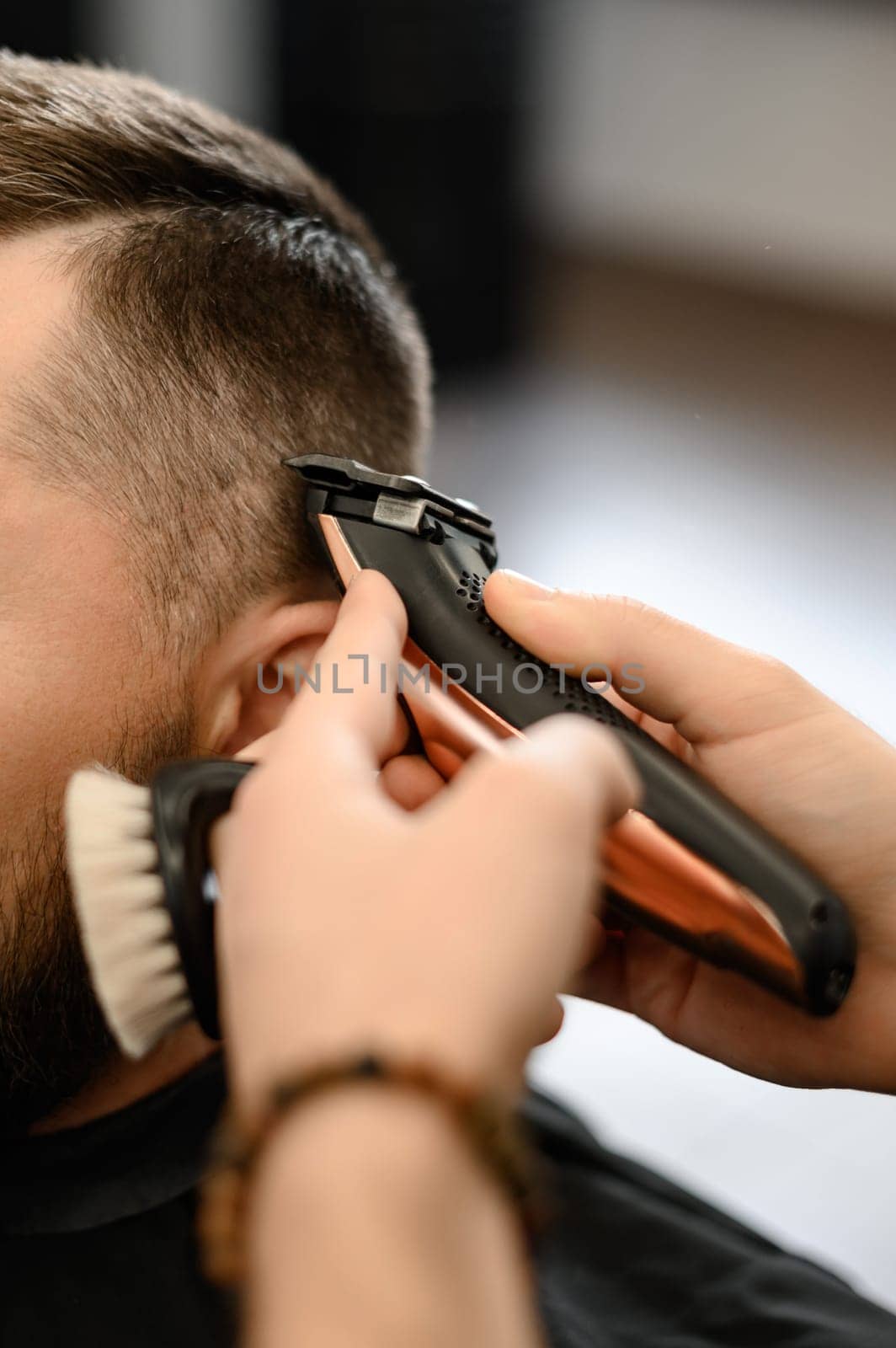 Barber shaves the contour of the oval line with a clipper on the client head. A man with a beard gets a haircut in a barbershop chair. by Niko_Cingaryuk