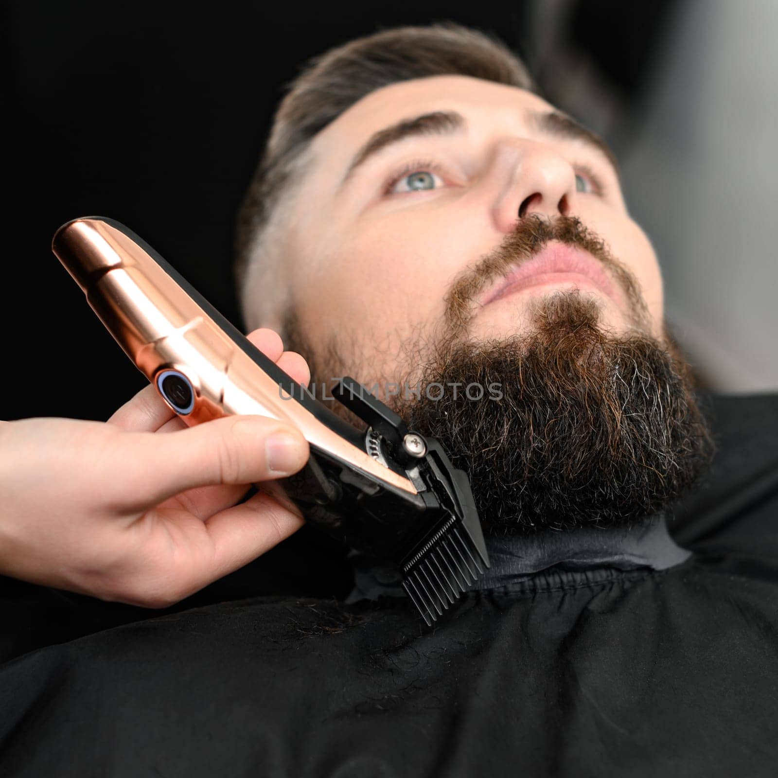Cutting a gentlemans beard in a barbershop with a clipper. Shortening the length of the beard from the sides by the master for the client. by Niko_Cingaryuk