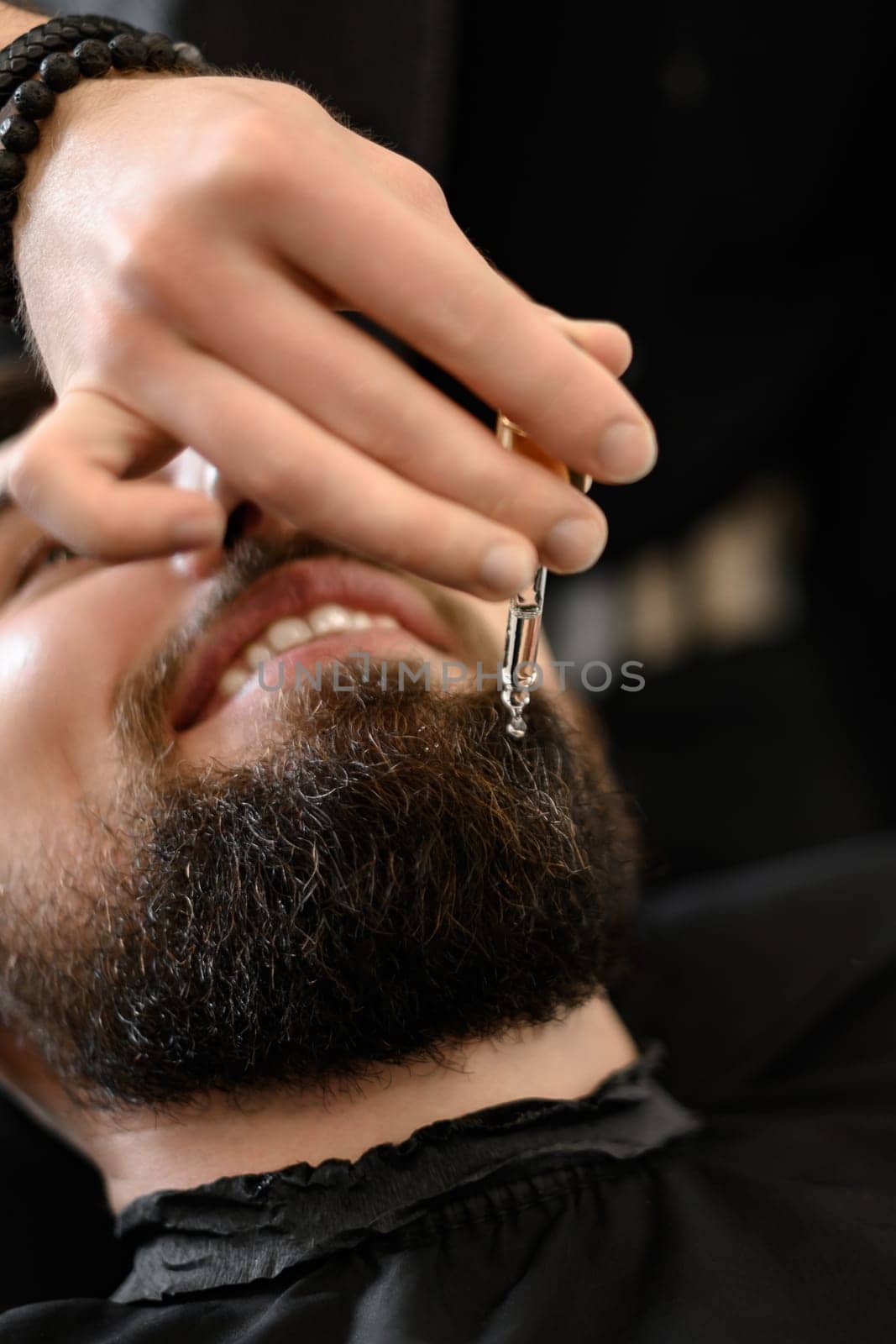 A barber stylist applies drops of oil to the clients beard to moisturize and soften. Beard care.
