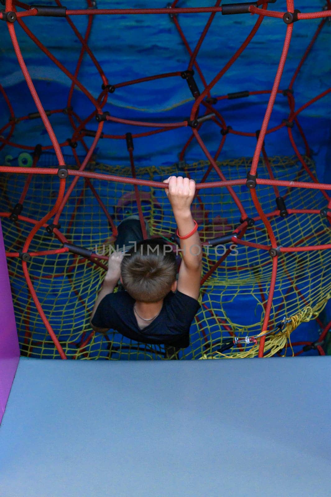 The boy climbs up the labyrinth with a web, children's activity in the playroom.