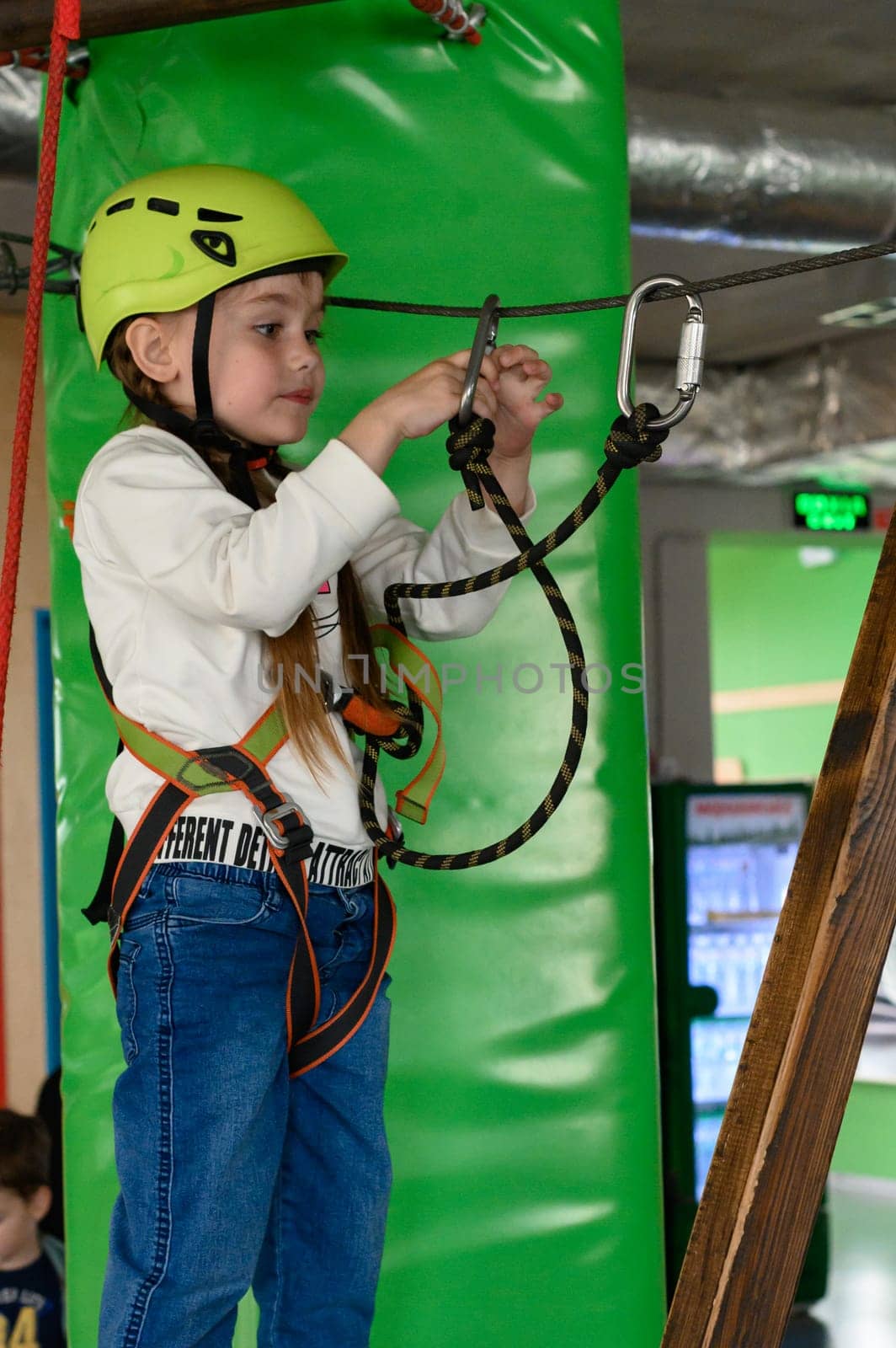 A little girl refastens a carabiner to another cable to go through another section of the cableway, active recreation for children.