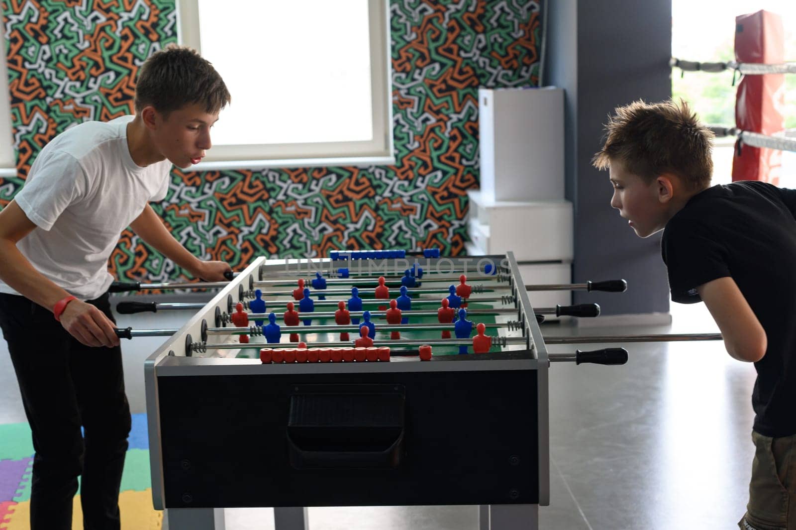 Two boys are playing table football in the playroom by Niko_Cingaryuk